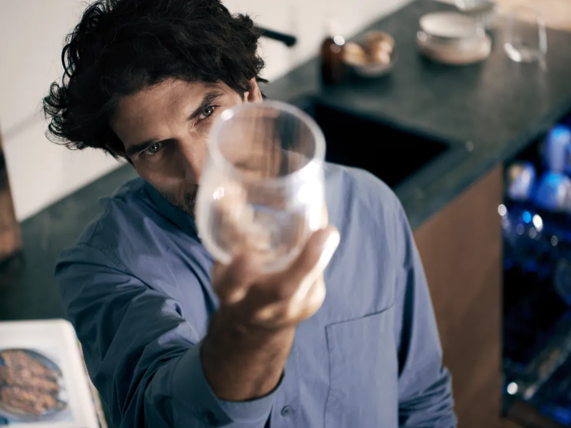Person holding a smartphone with screen visible, sitting with crossed legs indoors.