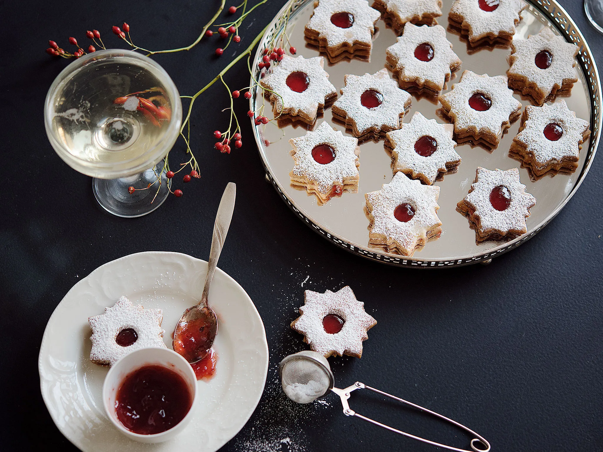 Festive Christmas cookies, jam-filled, powdered sugar, wine glass, holiday decor, baking tools.
