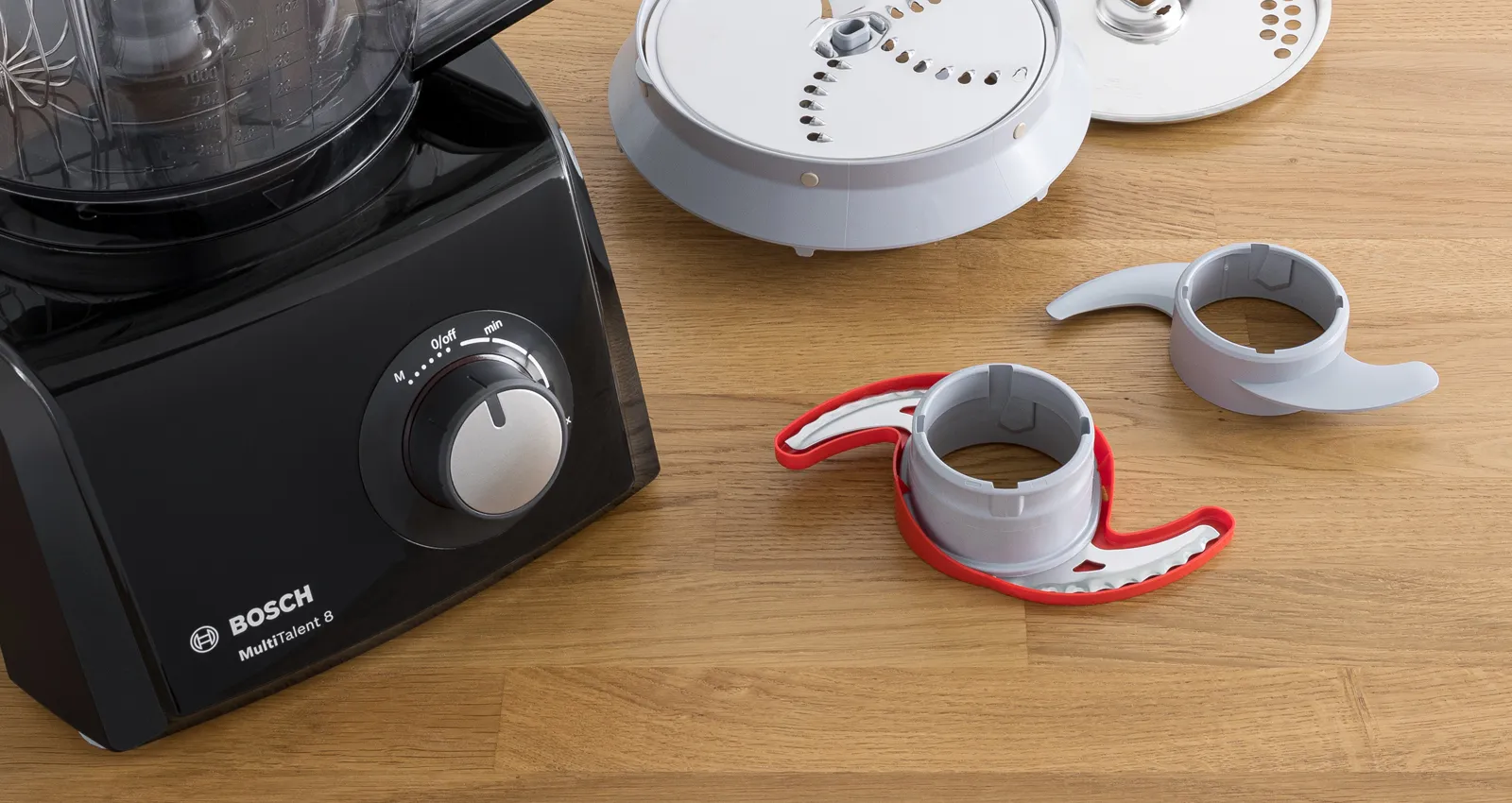 Un robot culinaire Bosch MultiTalent 8 noir sur une surface en bois, avec divers accessoires, y compris des composants de découpe et de mélange.