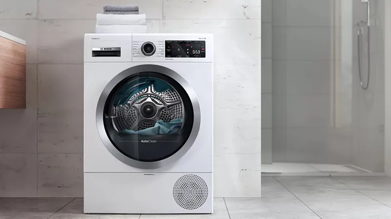 White front-loading clothes dryer with digital display and control panel in modern bathroom setting.