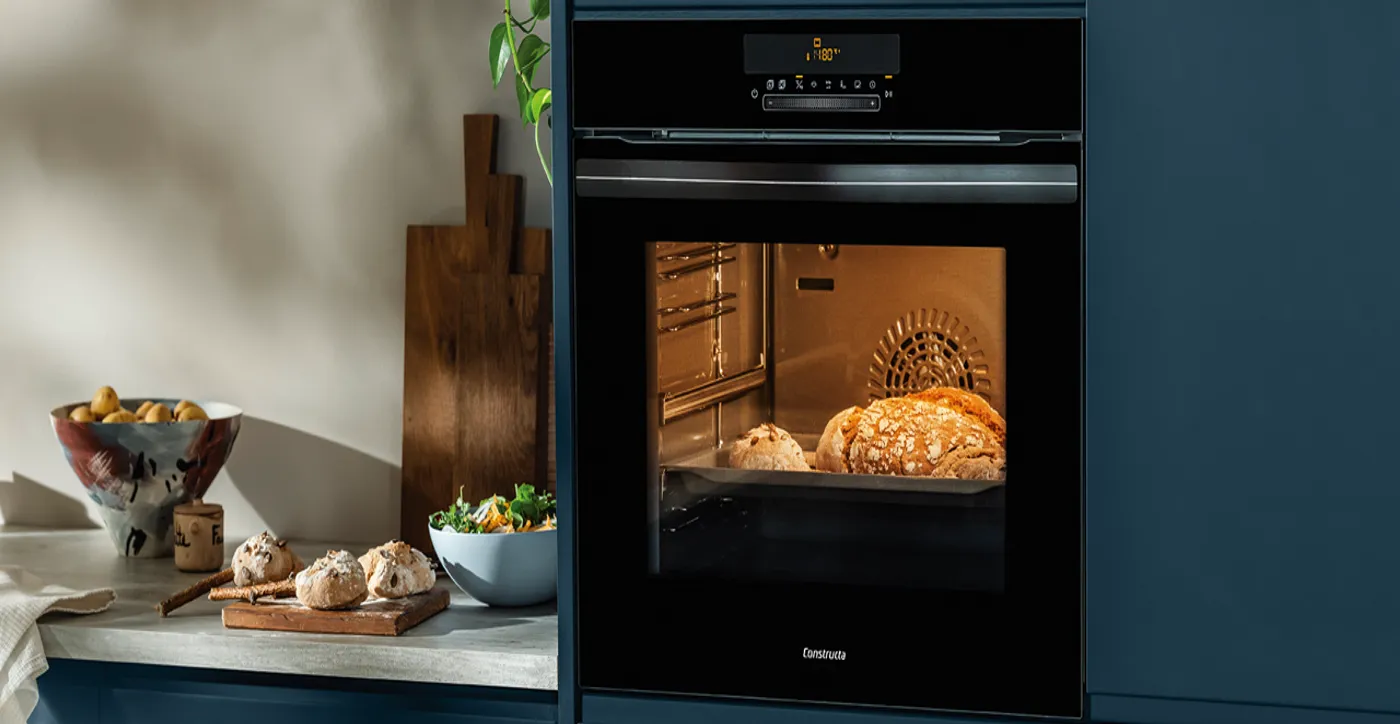 Ein Ofen, der frisch gebackenes Brot zeigt, umgeben von einer Schüssel Salat und einer Obstschale auf einer Küchenarbeitsplatte.