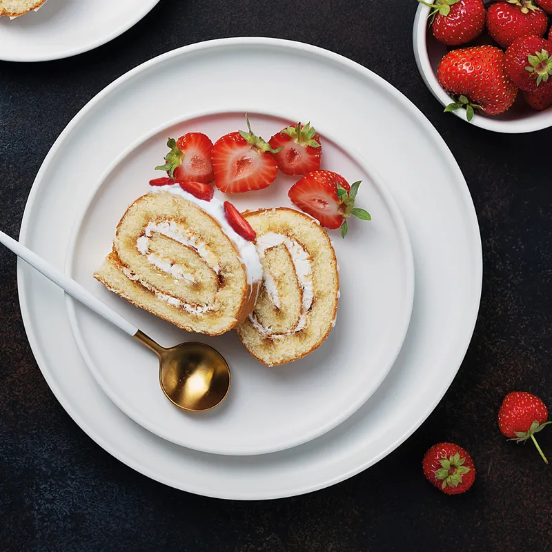 Sliced sponge cake roll with fresh strawberries, served on a white plate with a golden spoon.