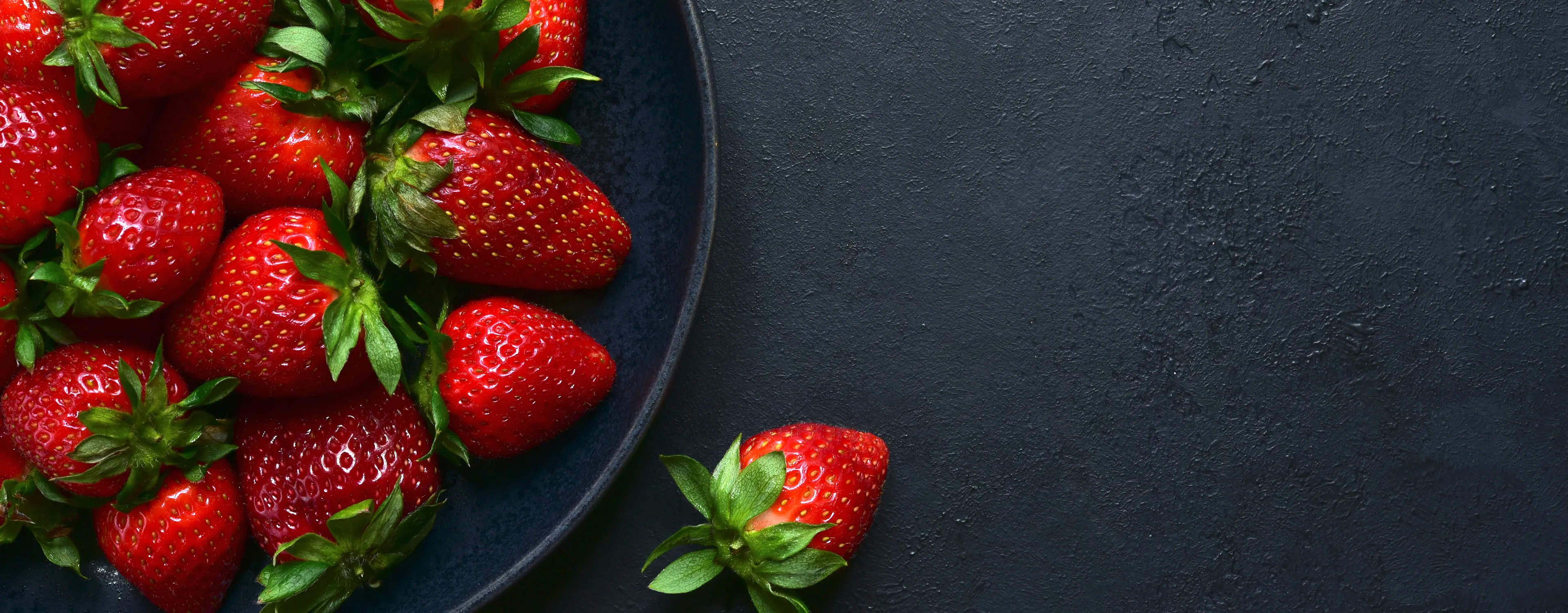 Fresh ripe strawberries arranged in a black bowl, ready to be enjoyed.