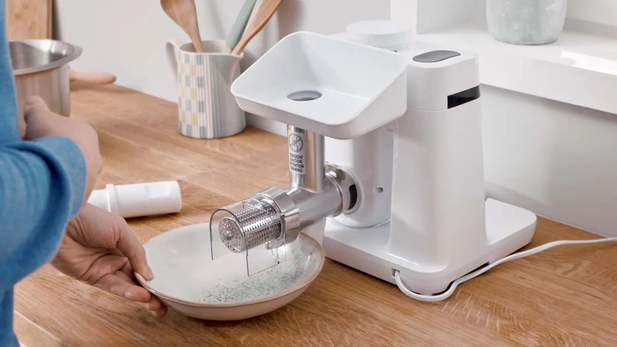 Kitchen appliance, electric meat grinder, mixing bowl, wooden table, cooking utensils.