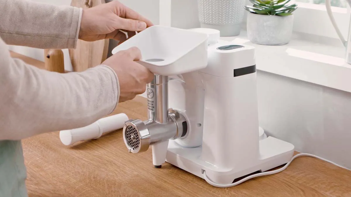 Person using a white electric meat grinder on a wooden table with a potted plant in the background.