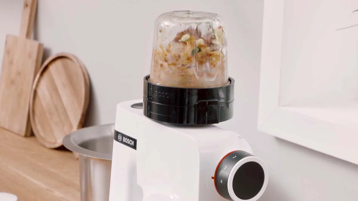 Blender with glass container filled with chopped ingredients on a wooden kitchen counter.