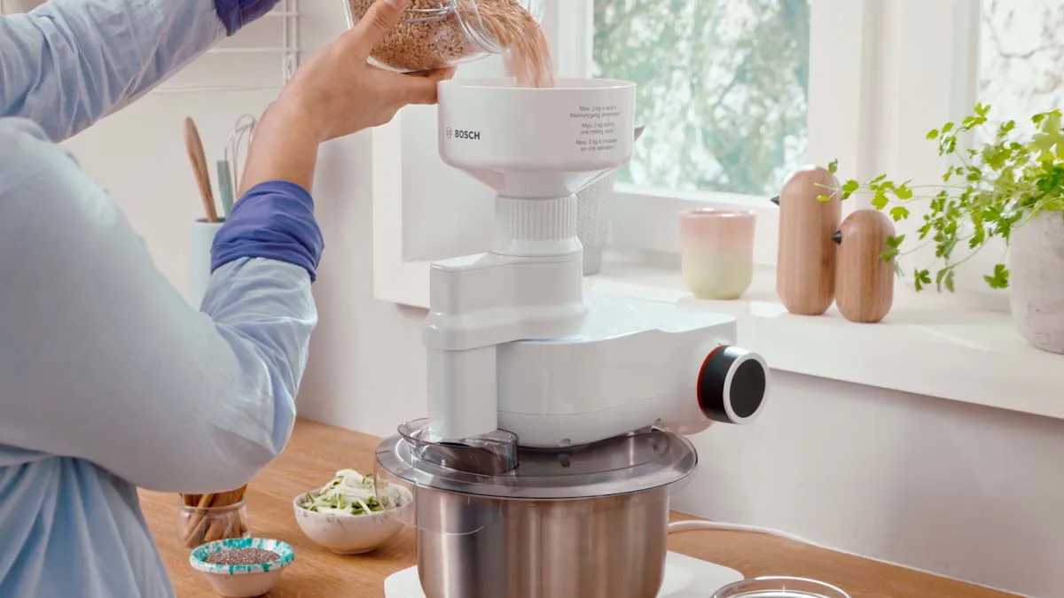 Woman using food processor in kitchen, preparing ingredients on counter.