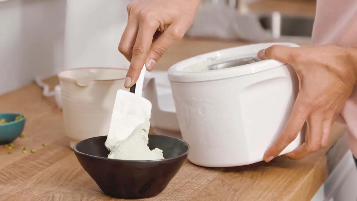 Hands mixing ingredients in a bowl and pouring from a container on a wooden surface.