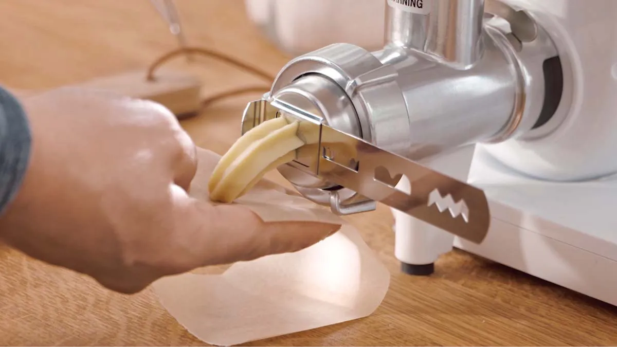 A person using a food processor to slice a lemon on a wooden surface.