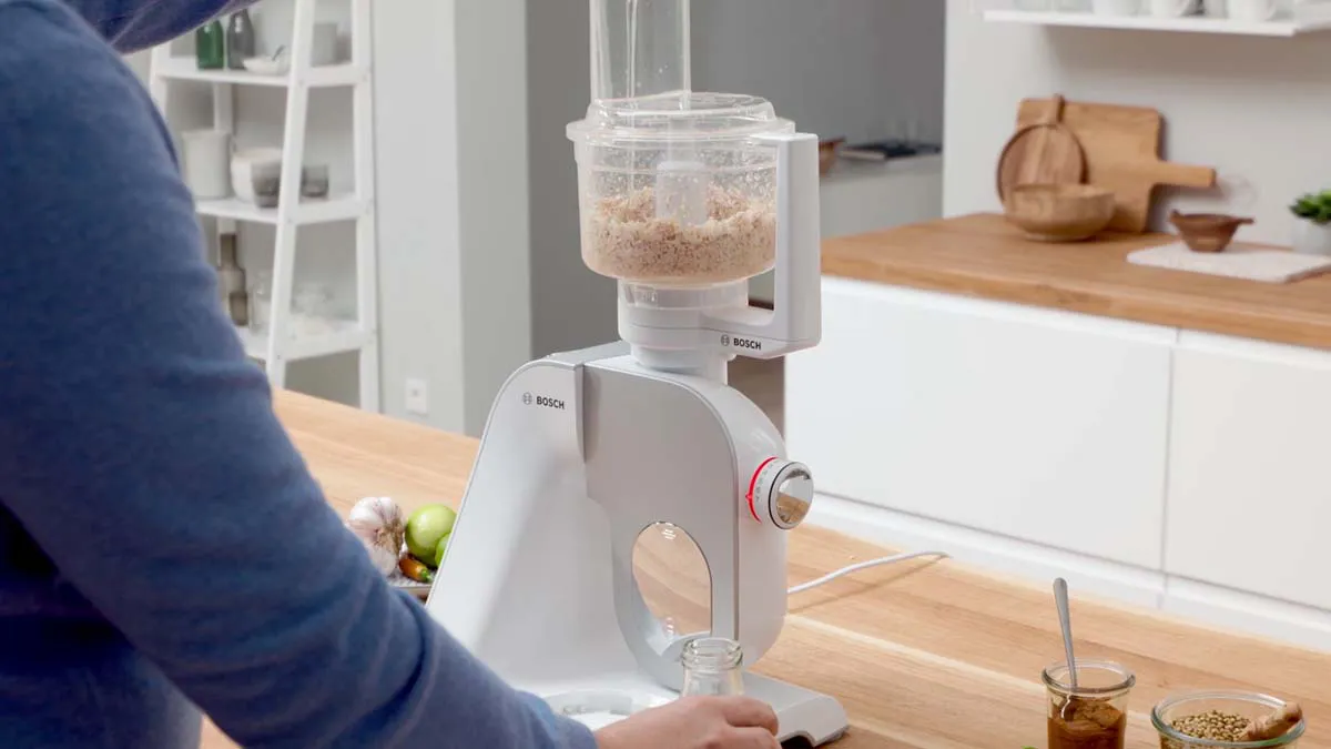 Person using a white electric food processor in a modern kitchen.