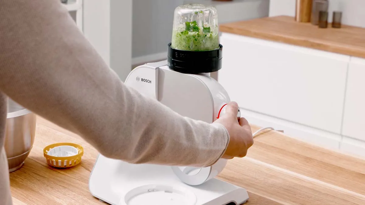 Kitchen appliance, food processor, chopping greens, wooden countertop, kitchen interior.