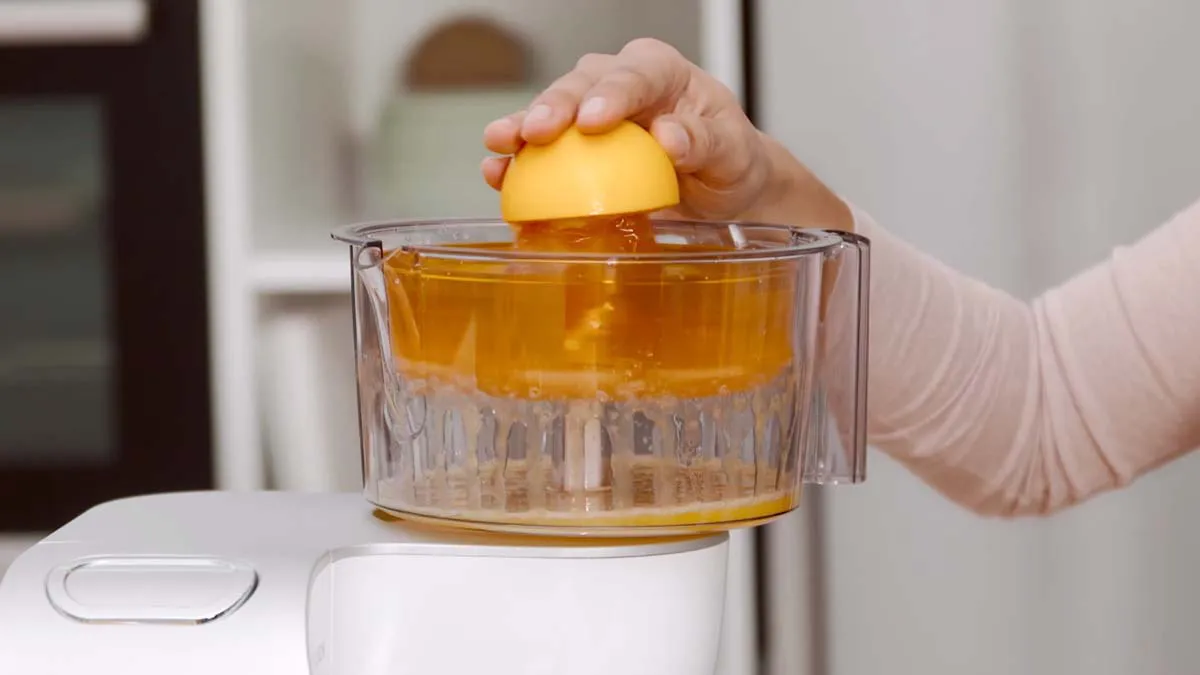 Hand squeezing lemon over glass container filled with liquid.