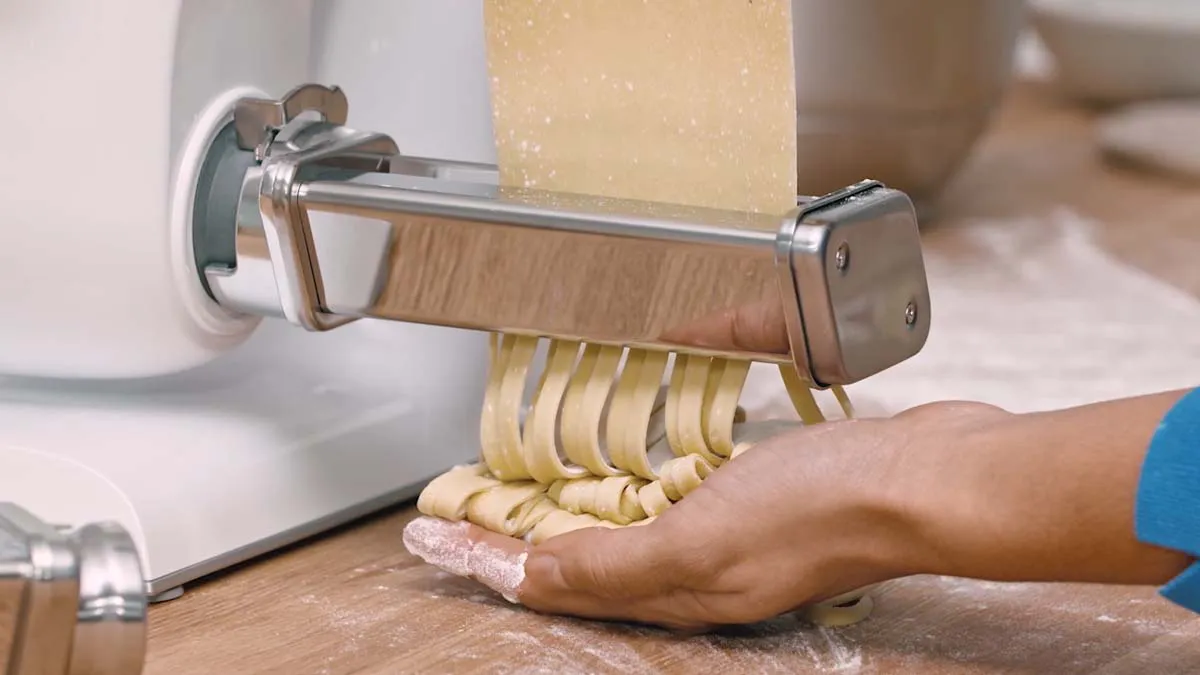 Pasta maker machine extruding fresh homemade pasta dough on wooden surface.