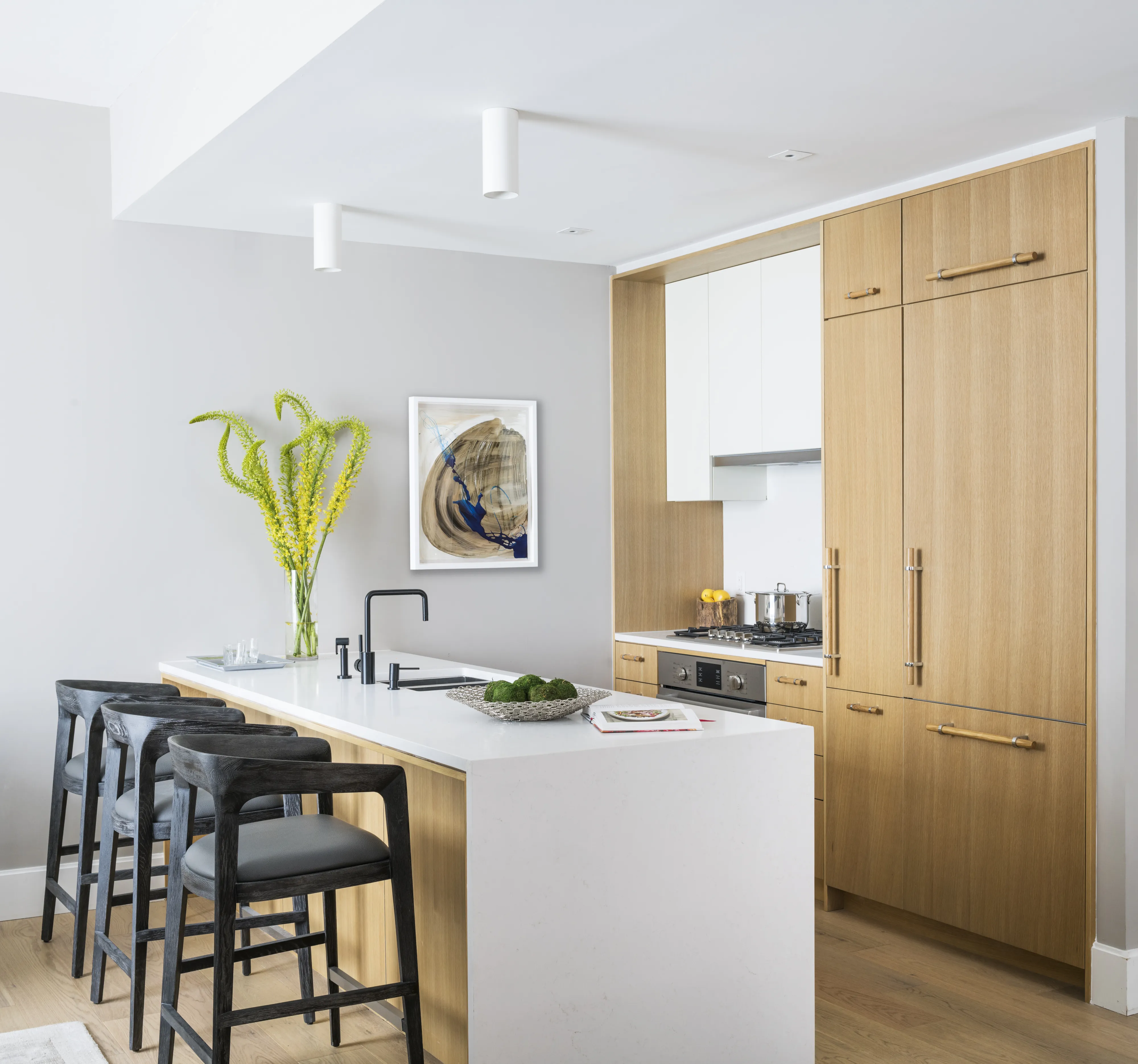Modern kitchen with Bosch gas range, wood cabinets, island bar, black stools, and decorative artwork.