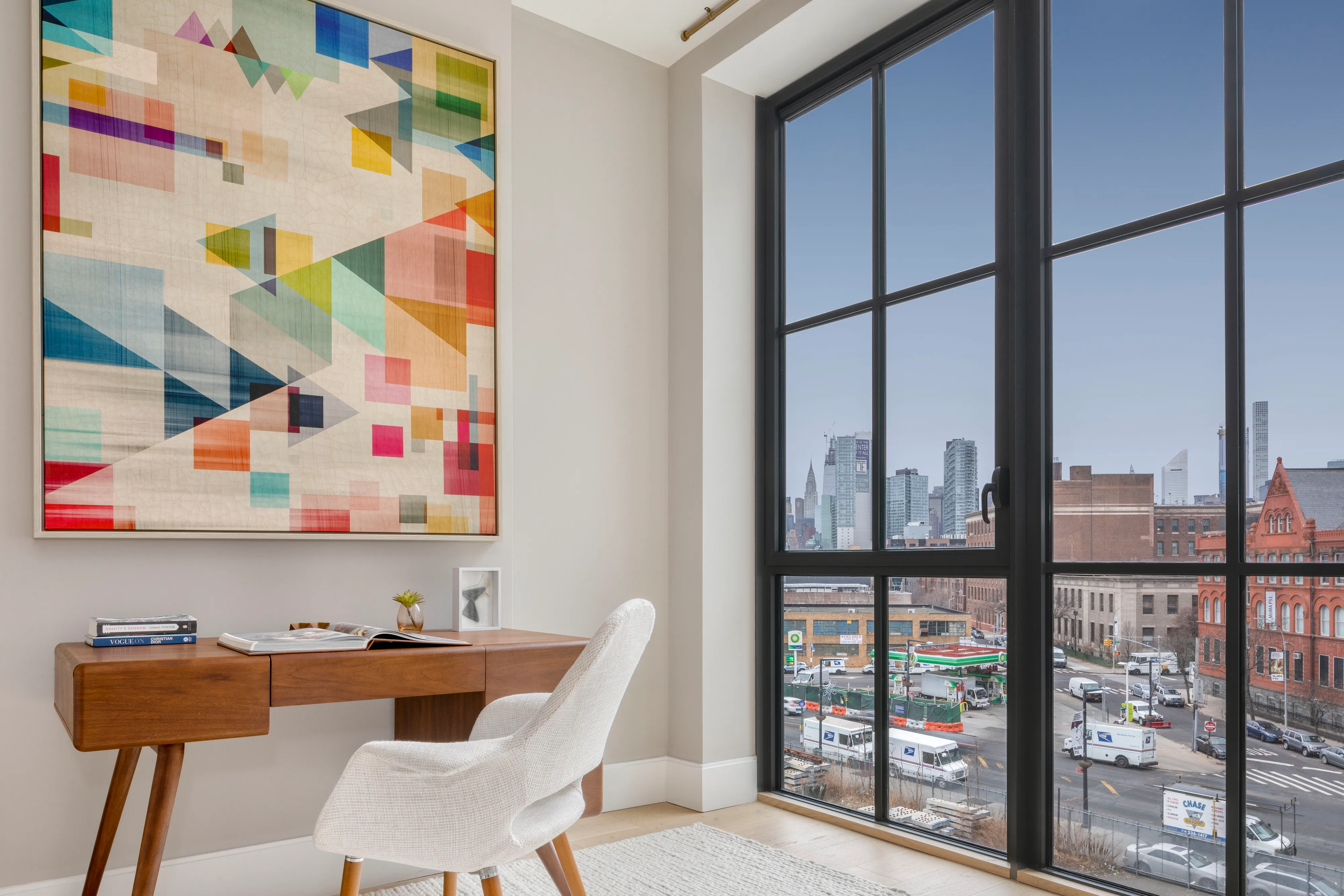 Modern home office with a wooden desk, abstract art, and a large window with city view.
