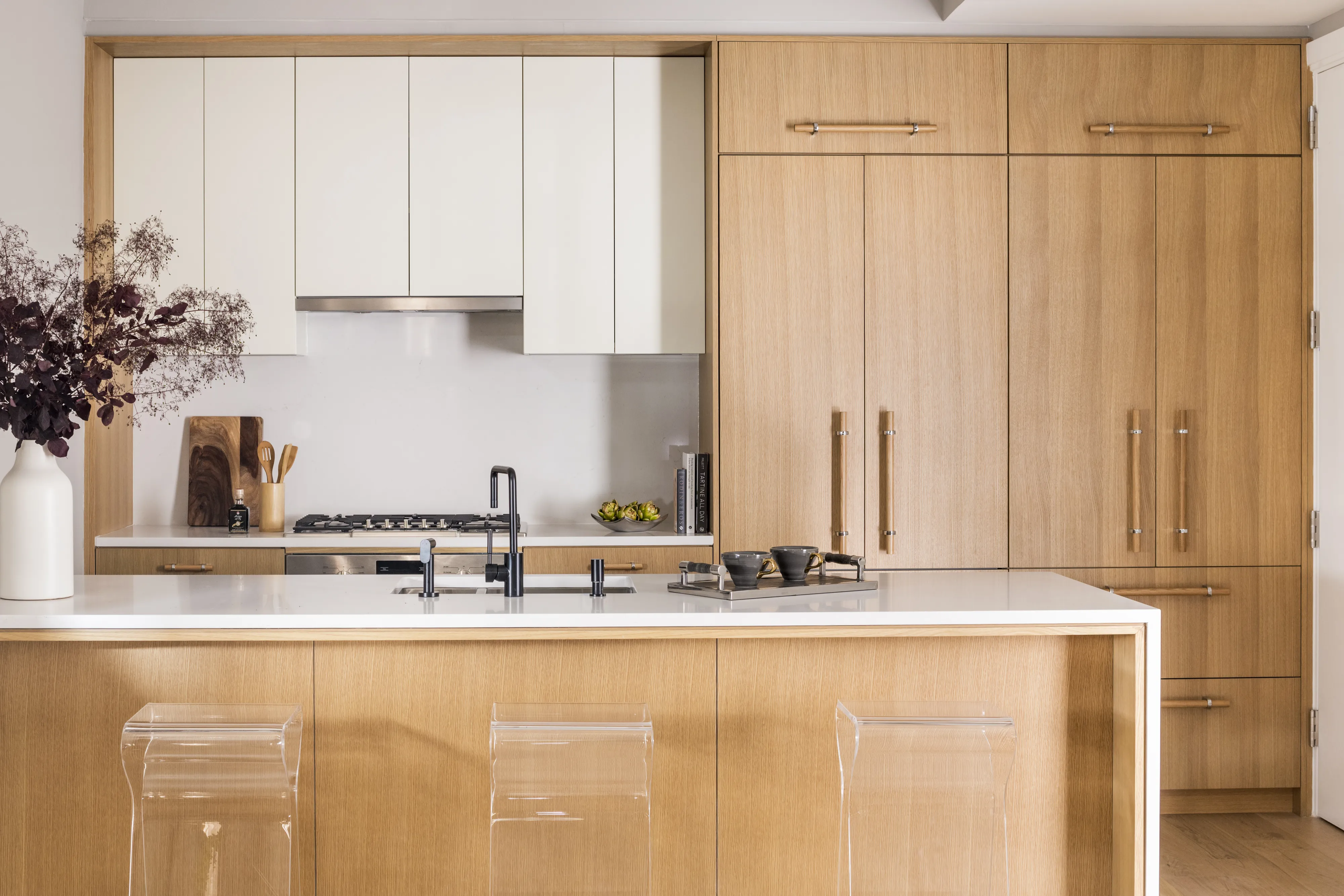 Modern kitchen with Bosch gas range, wood cabinetry, white island, and transparent stools.