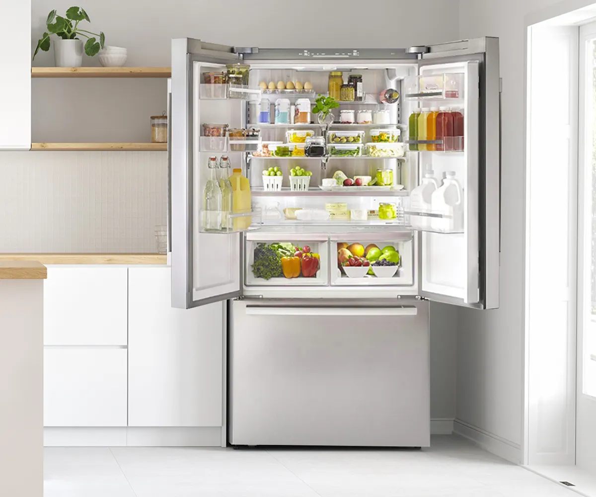 Open refrigerator filled with various food items, including fruits, vegetables, and condiments, in a modern kitchen setting.