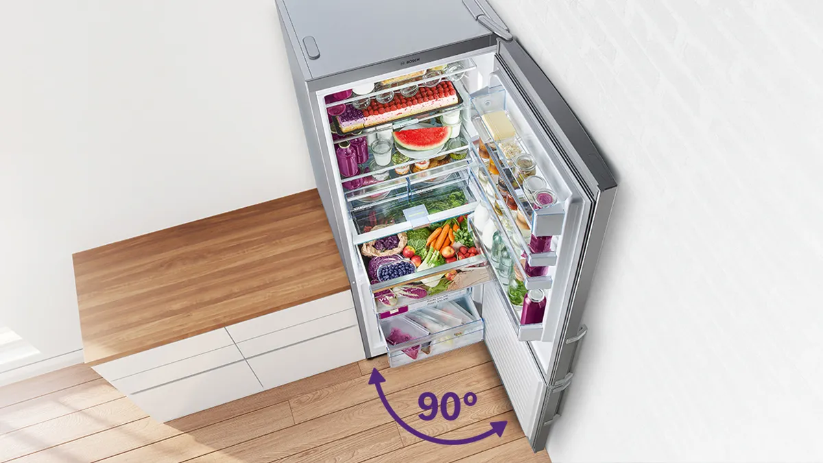 ثلاجة Bosch PerfectFit ذات الباب المفتوح بزاوية 90 درجة، تُظهر إمكانية الوصول الكامل إليها حتى عند وضعها بجوار طاولة المطبخ، وهي مليئة بالأطعمة الطازجة المتنوعة على أرفف متعددة وفي صناديق الباب.
