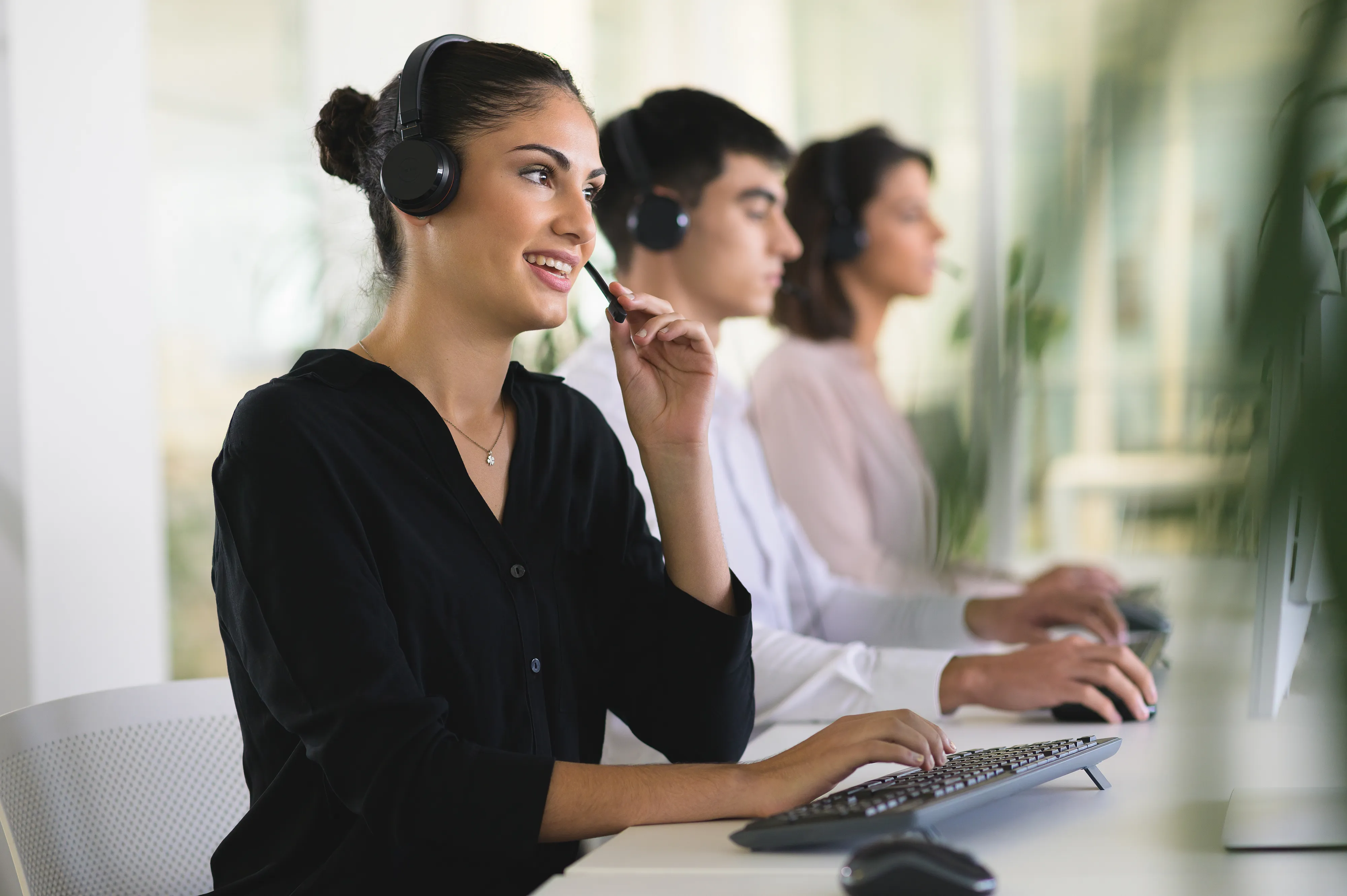 Three customer service representatives working at computers with headsets.