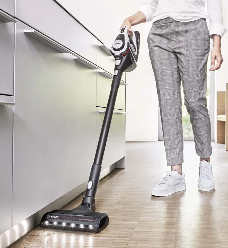 A woman uses a cordless vacuum to clean up a mess on a cream rug in light, bright living room.