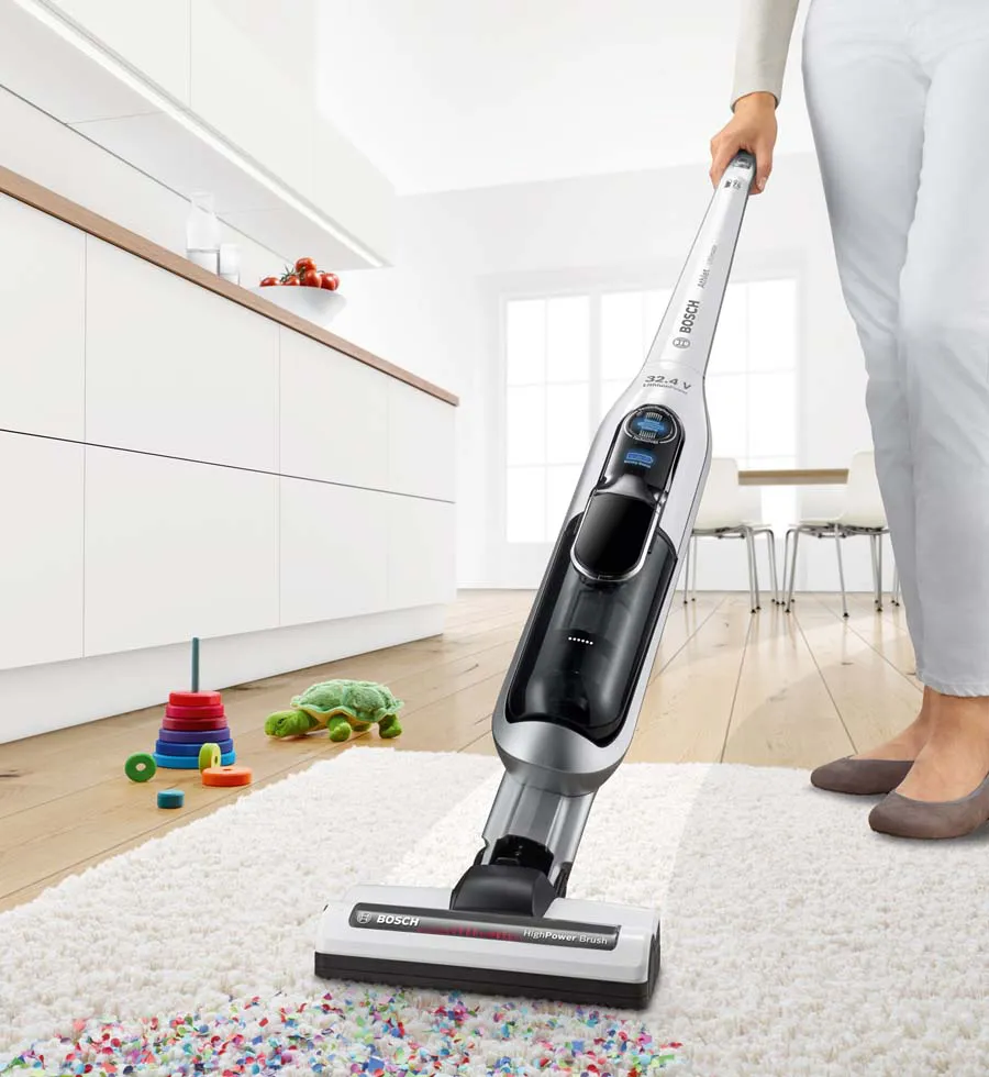 A woman uses a cordless vacuum to clean up a mess on a cream rug in light, bright living room.
