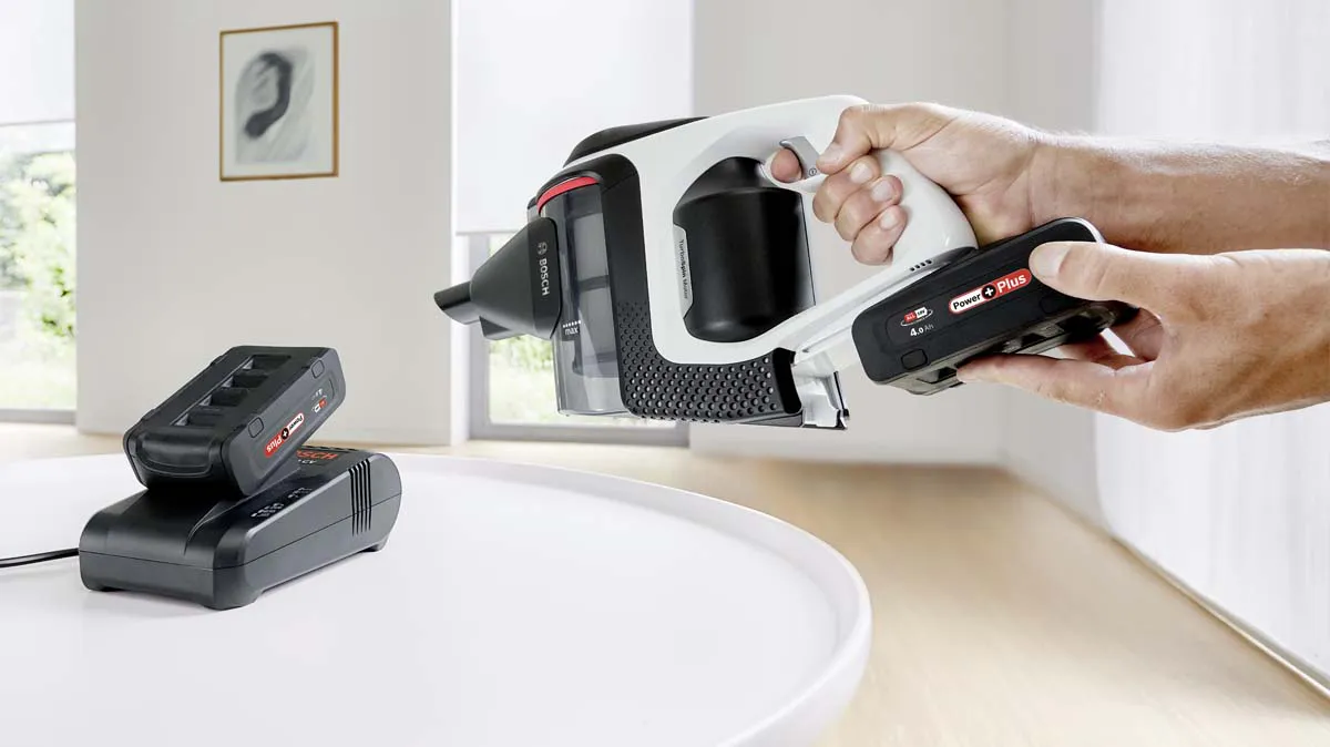 Clicking a battery into the Unlimited vacuum cleaner. A second battery charges in the fast charger.