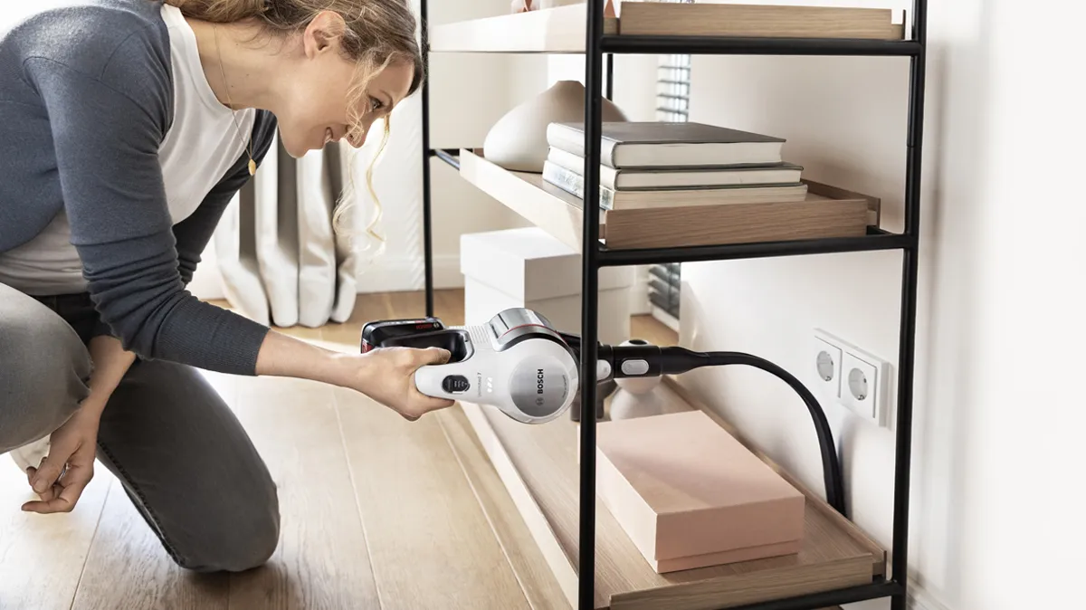 A woman uses a handheld cordless vacuum to remove dust.