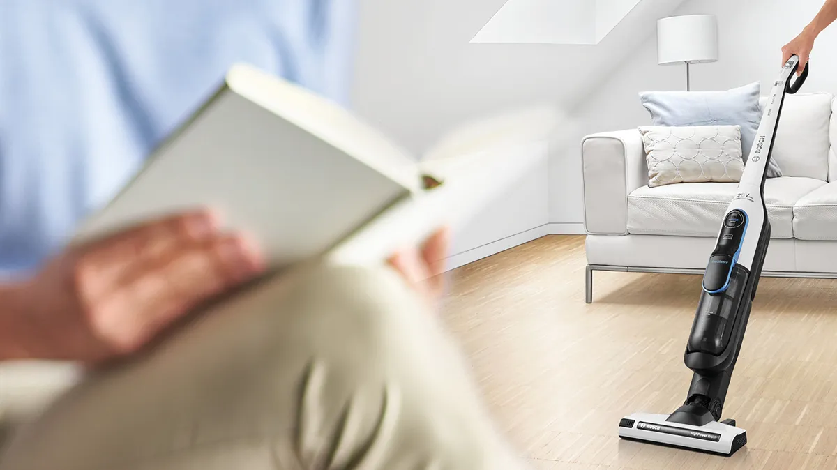 Person reads while someone vacuums in the background.