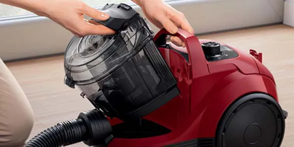 Person using a red canister vacuum cleaner on a wooden floor.