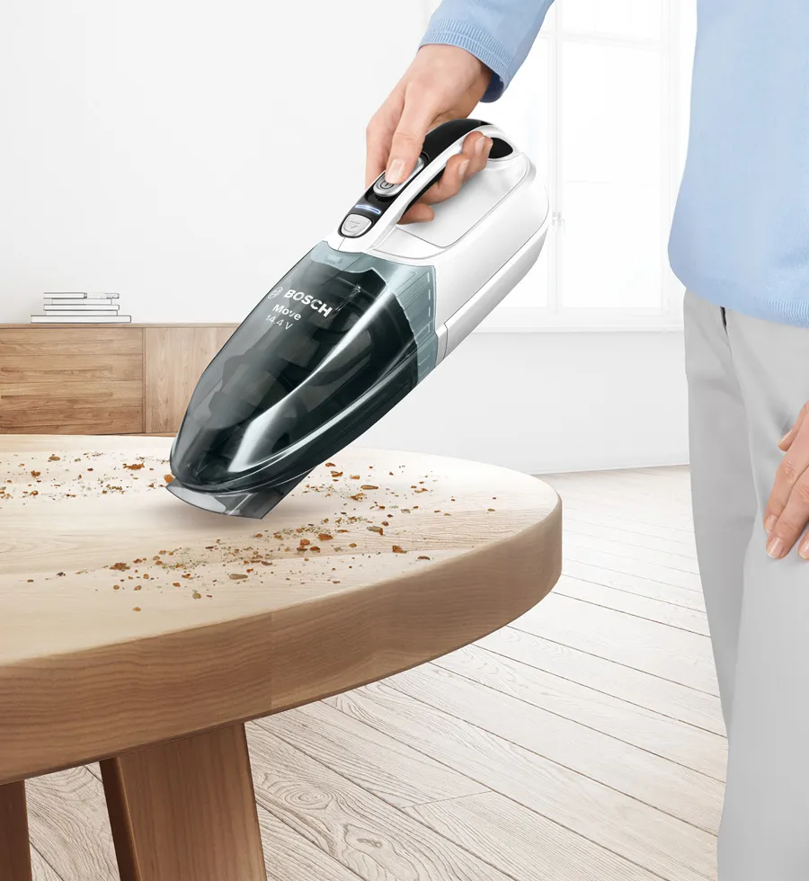 Person cleans up biscuit crumbs on a countertop with a handheld vacuum.