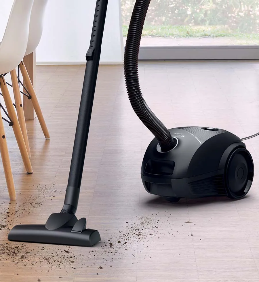 A woman uses a cordless vacuum to clean up a mess on a cream rug in light, bright living room.