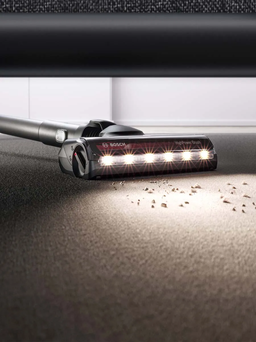 Vacuum cleaner in use on a surface with both wooden floor and carpet, cleaning various messes.