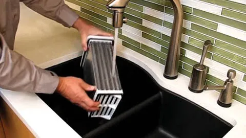 Hands washing something inside kitchen fauce, with a green tile backsplash.