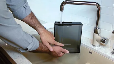 Person filling up coffee machine part with water from faucet