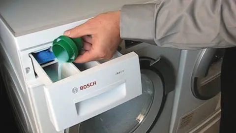 Person loading detergent into Bosch washing machine.