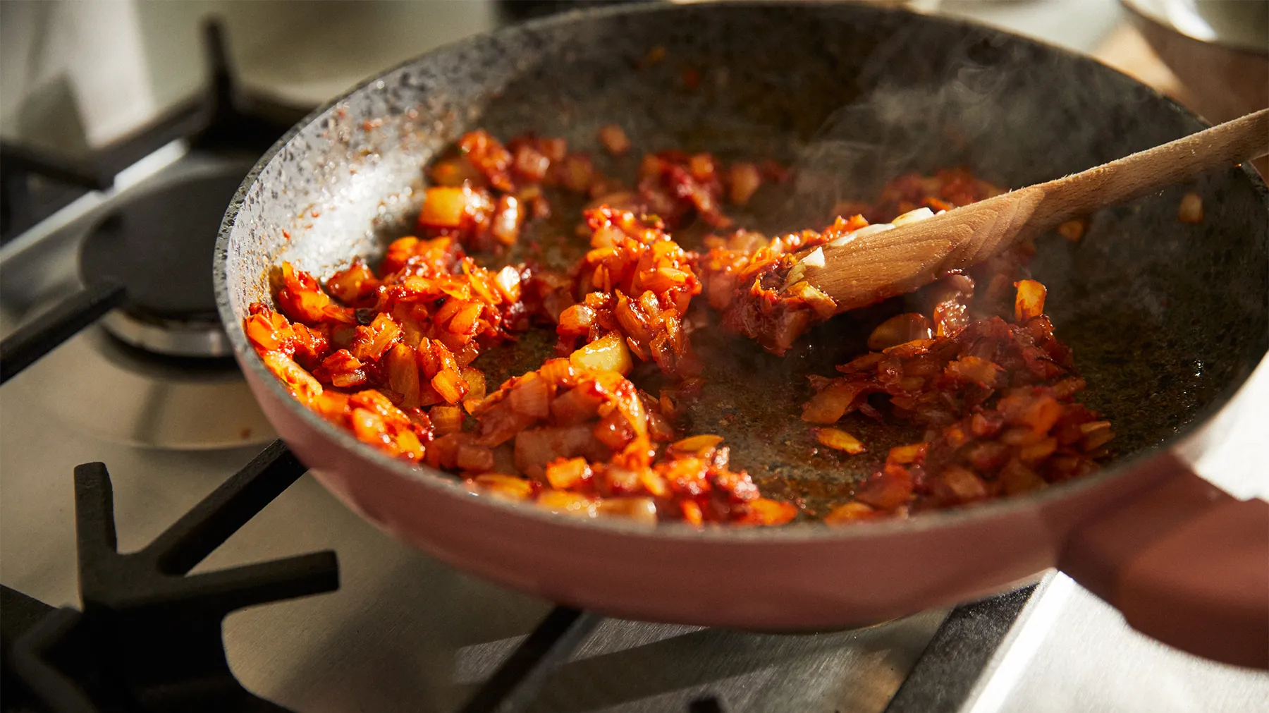 Sizzling pan of cooked ground meat and vegetables on a stovetop.