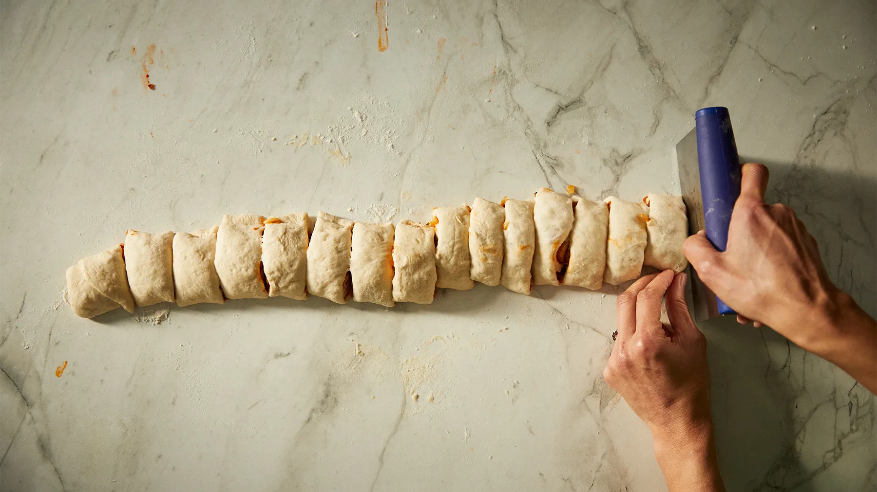 Hands rolling and shaping dough into a long, twisted bread on a marble surface.