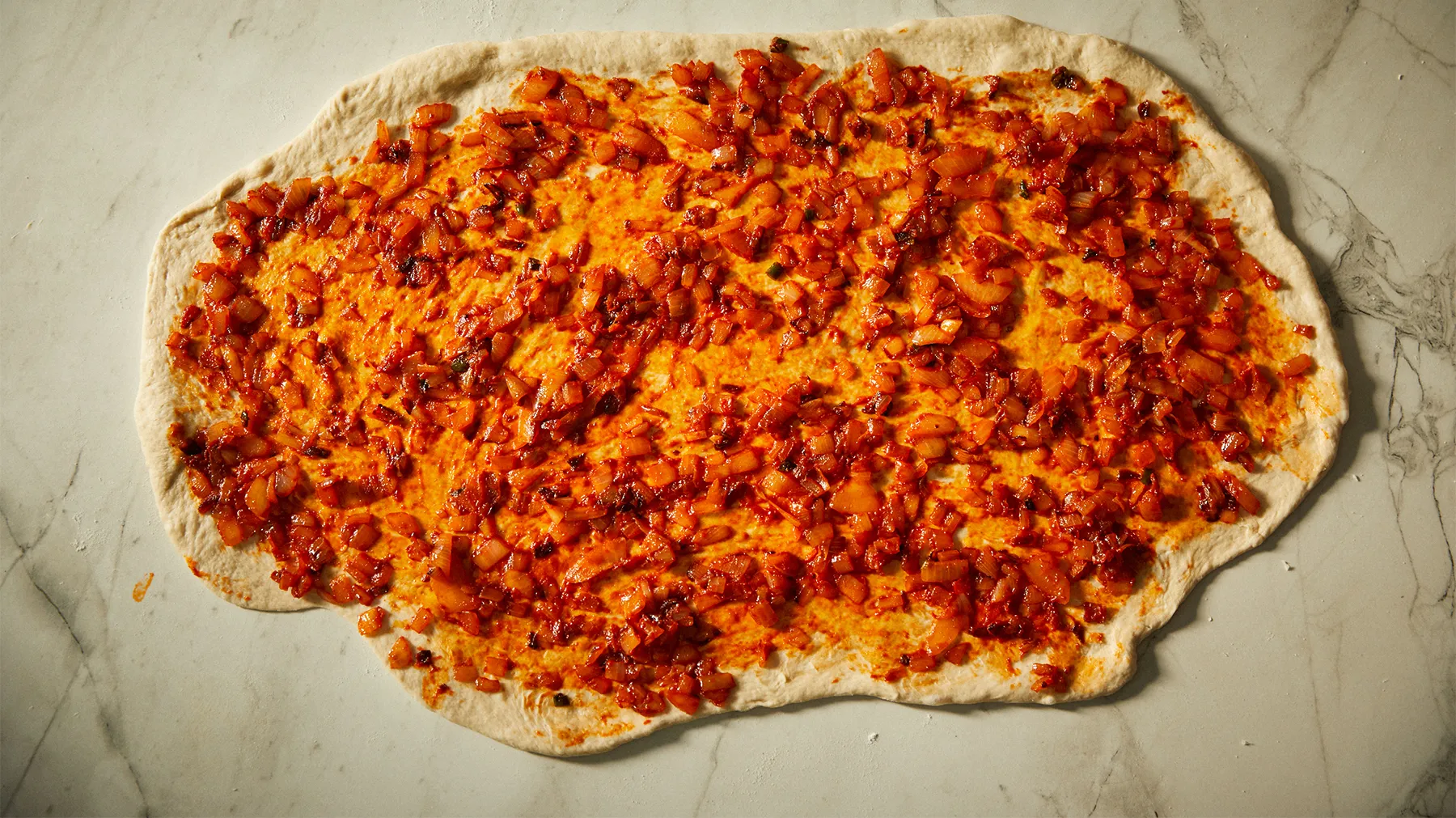 Flatbread topped with spicy, crumbled meat and melted cheese, ready for baking or serving.