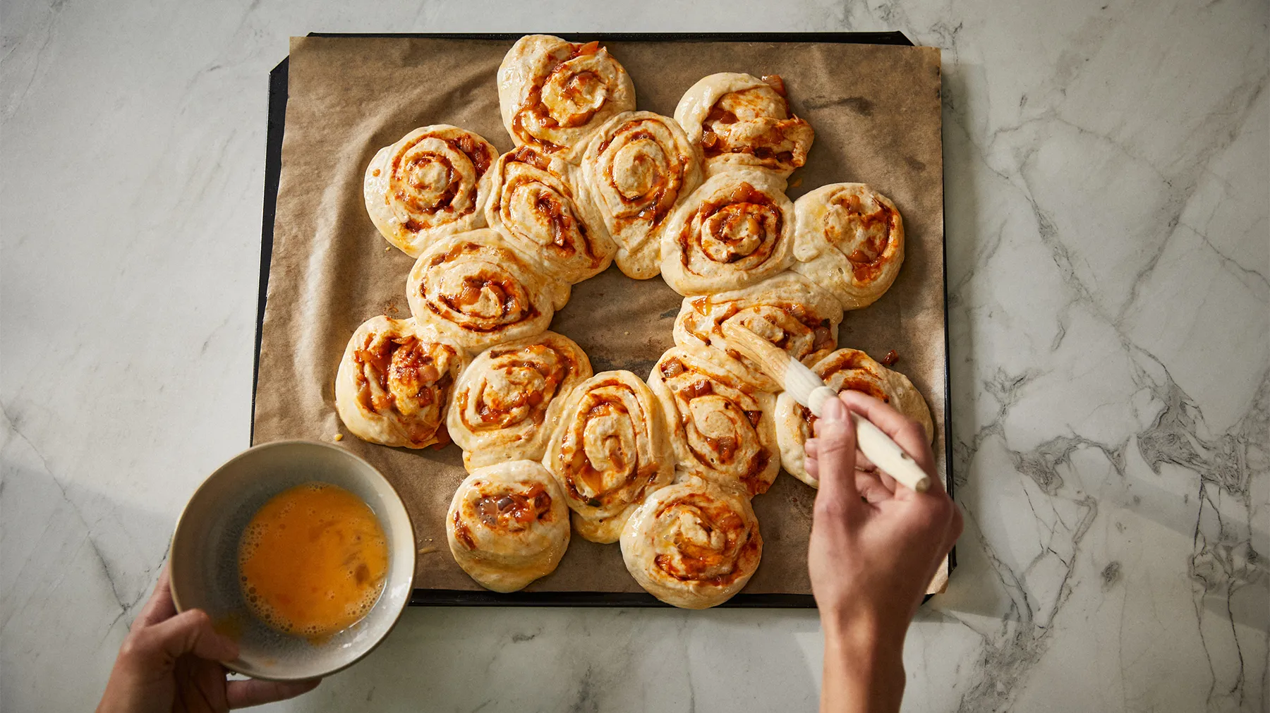 Freshly baked cinnamon rolls arranged on a baking sheet, with a hand reaching to grab one.