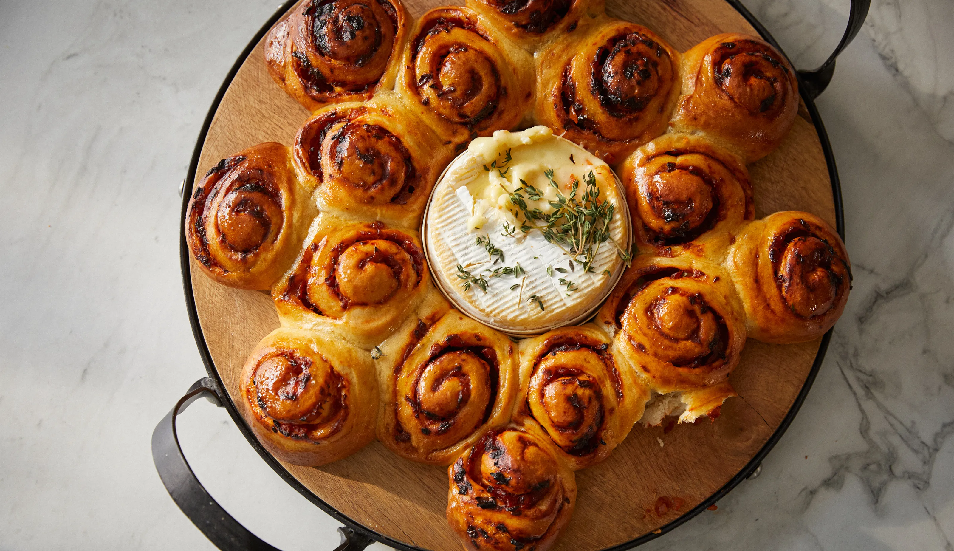 Freshly baked cinnamon rolls surrounding a creamy cheese dip, served on a marble surface.