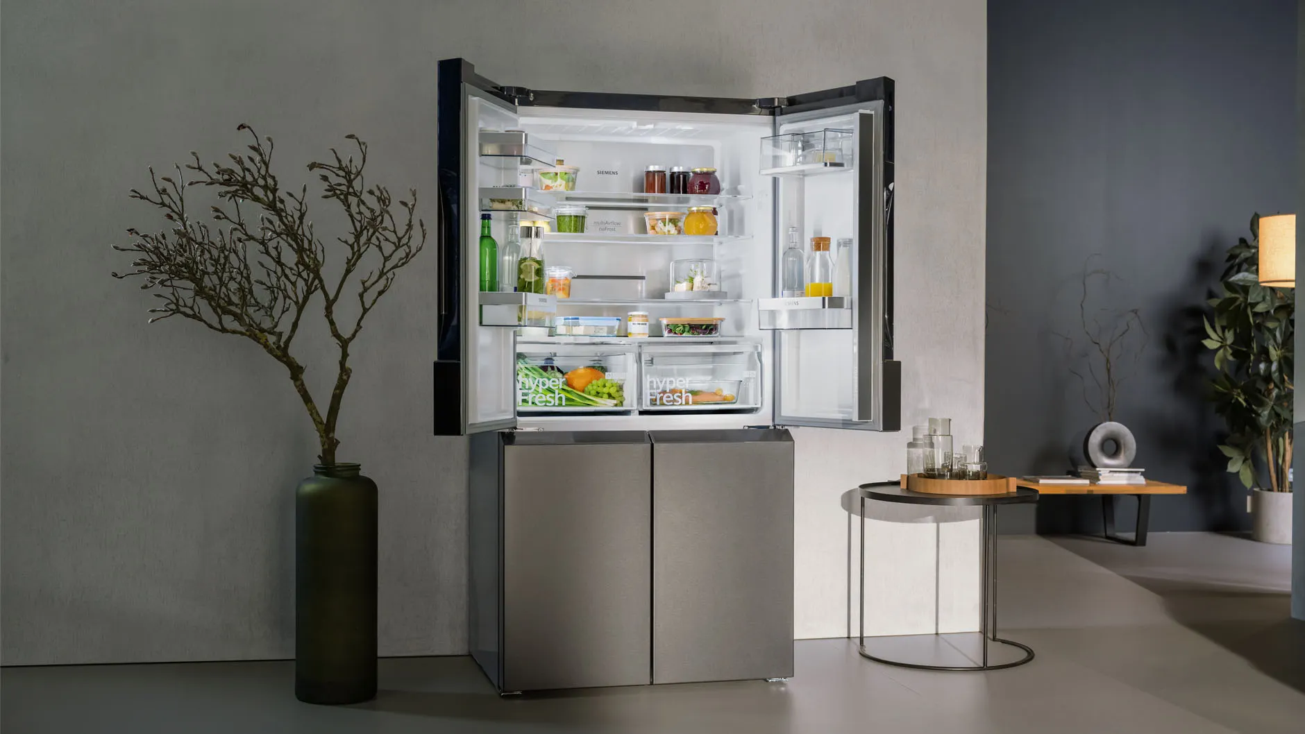 Open refrigerator with various food items, plant, and minimalist decor in modern kitchen setting.