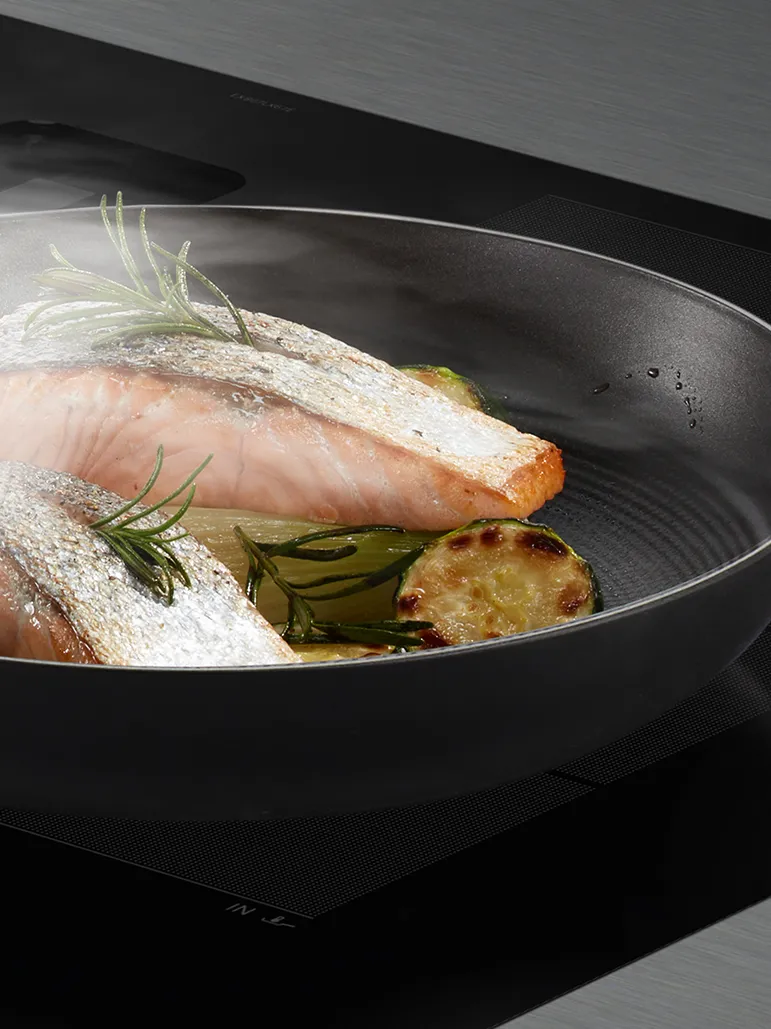 Filete de salmão assado com alecrim, limão e legumes assados em uma panela de cozinha escura.