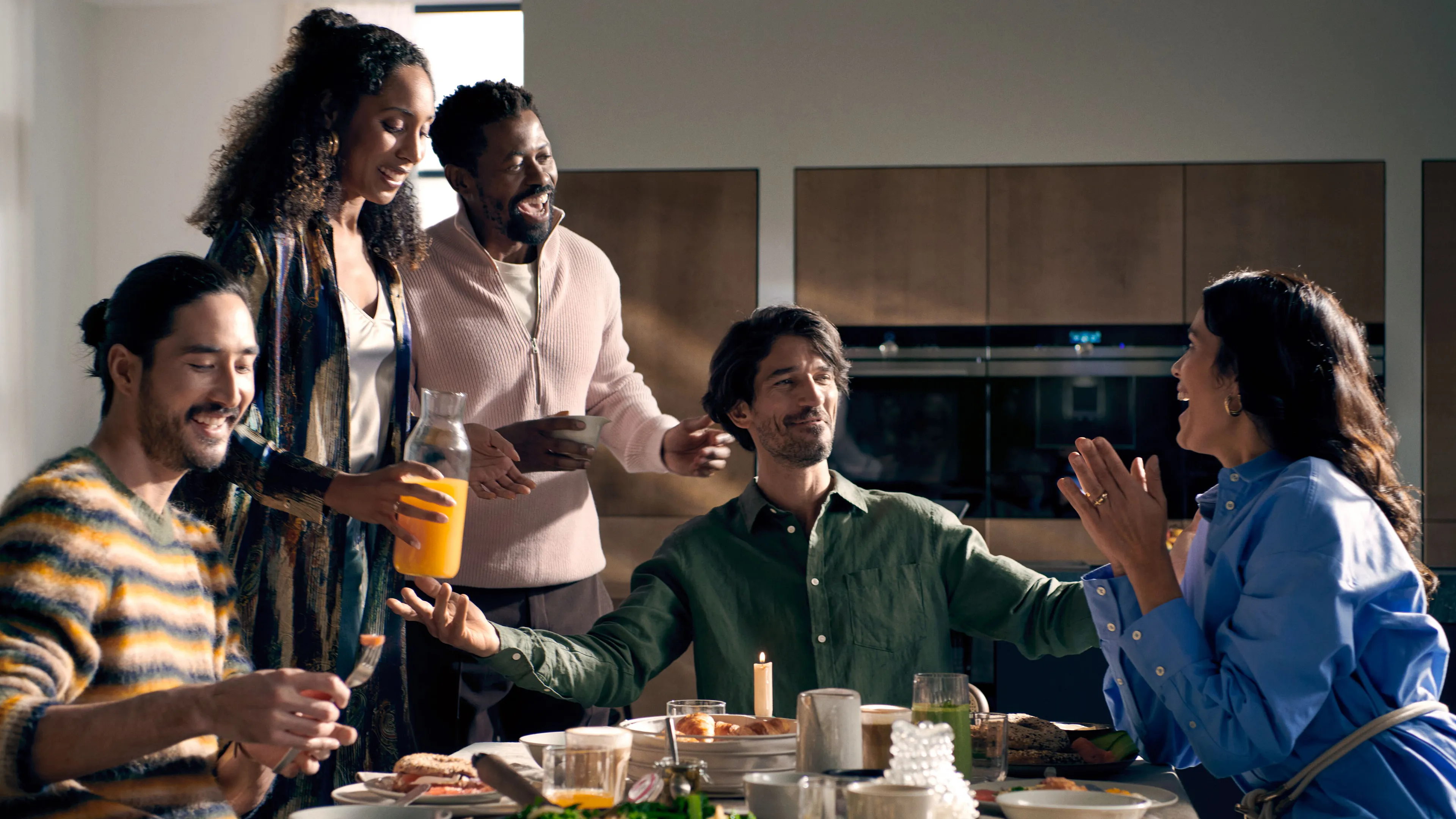 Group of friends enjoying a meal together, laughing and conversing in a home kitchen setting