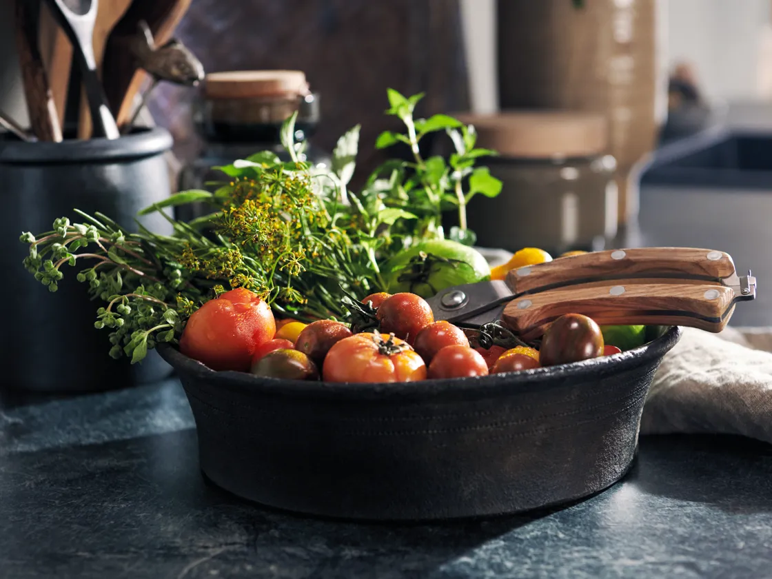 A variedade de vegetais frescos, ervas e utensílios de cozinha em uma superfície escura.