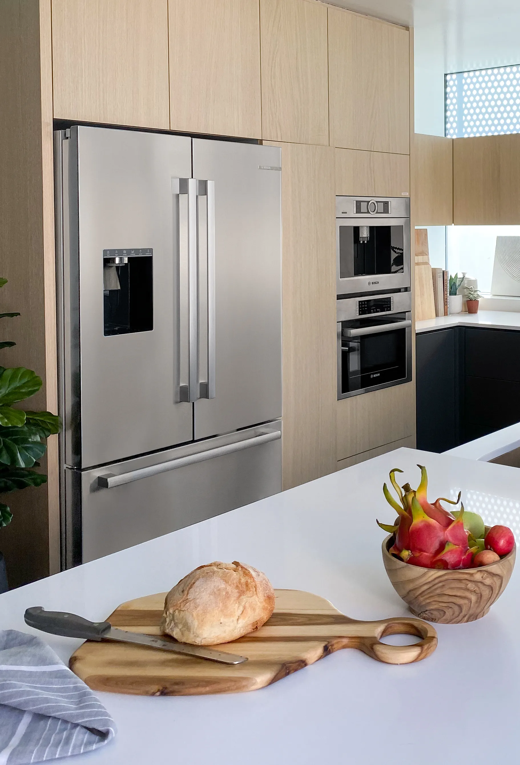 Modern kitchen with a stainless steel fridge and inbuilt Bosch oven, bread on counter.