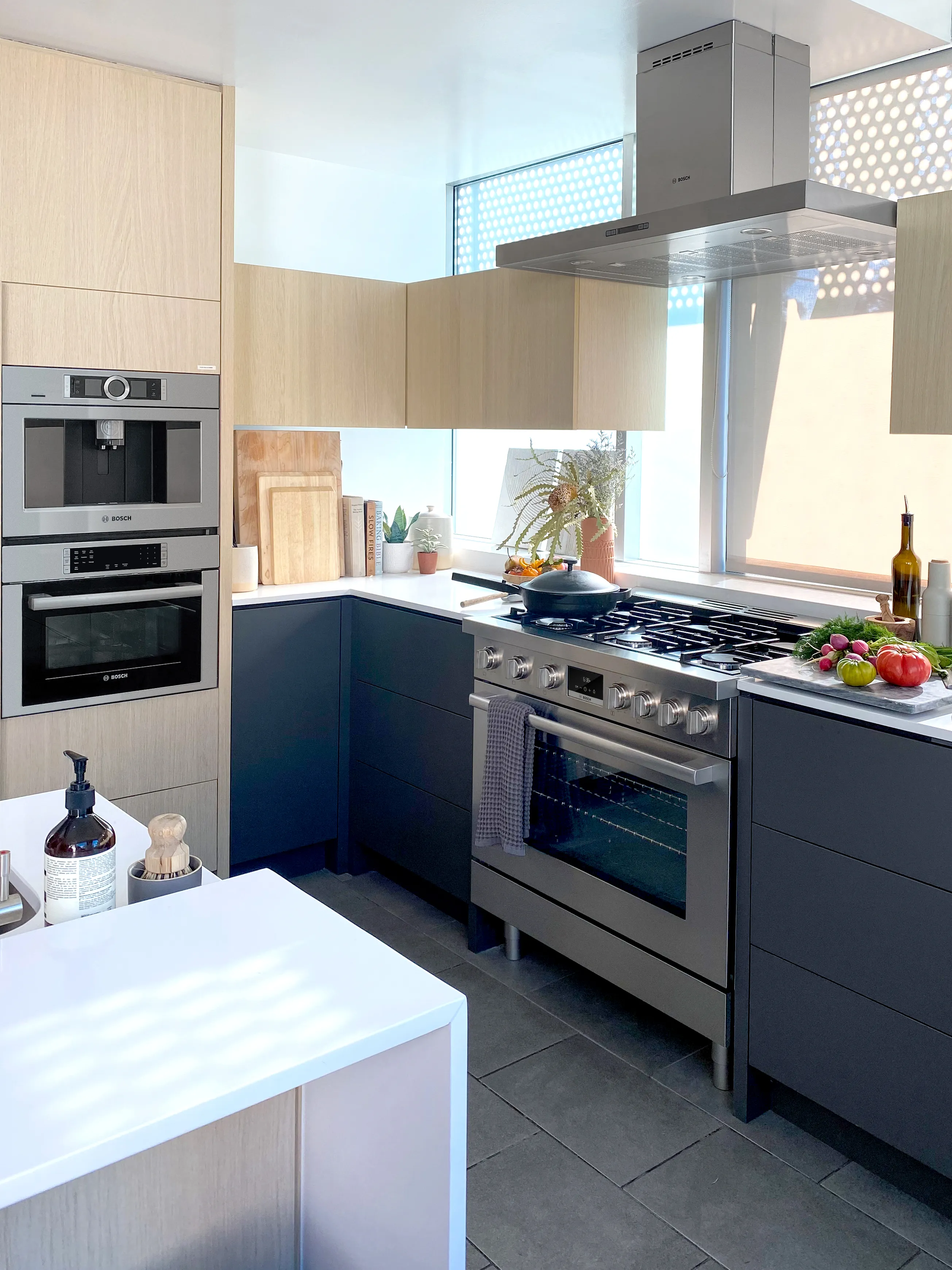 Modern kitchen with Bosch oven, stove, and stainless steel appliances, vegetables on counter.