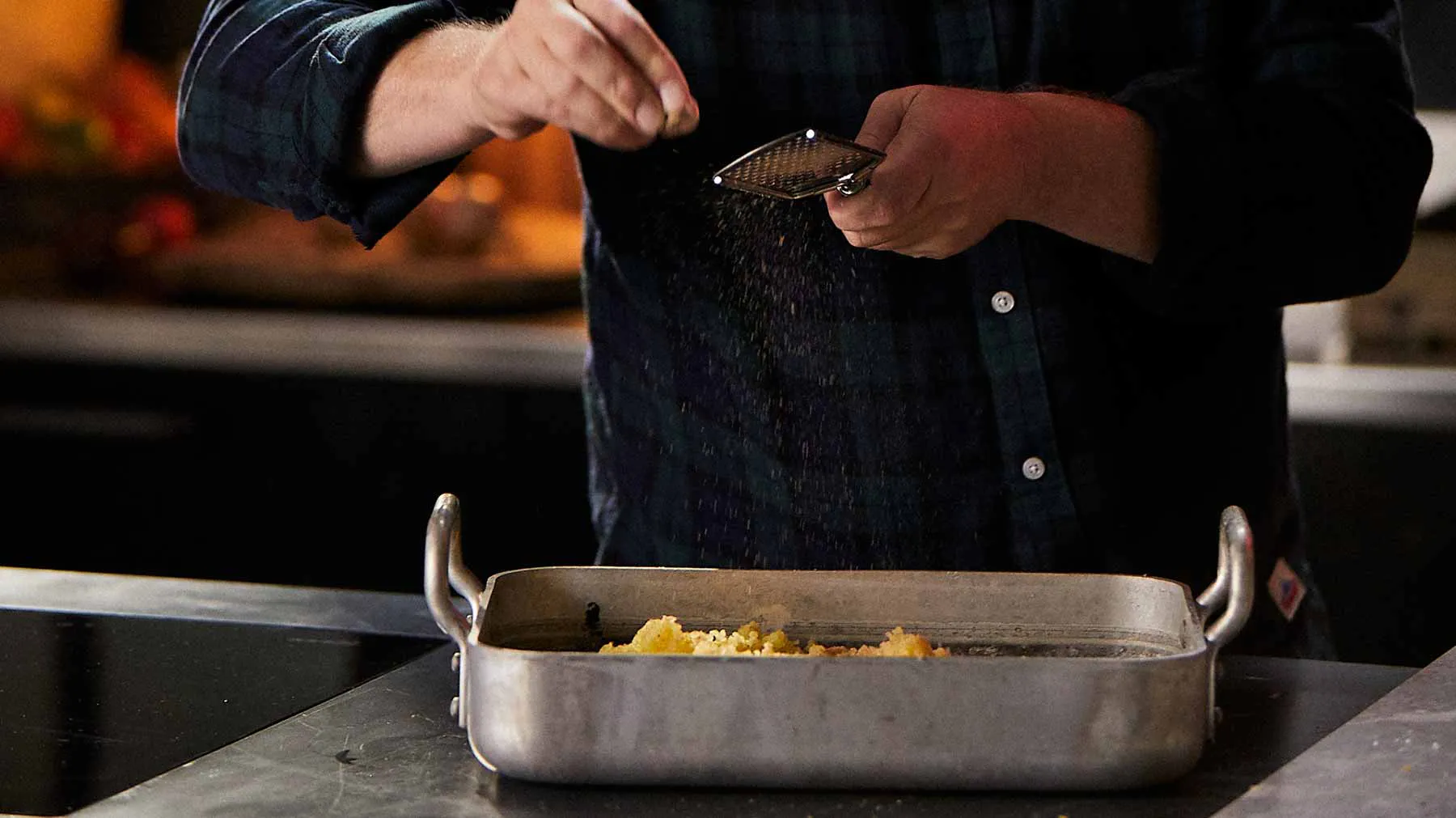 Chef seasoning food in baking tray on kitchen counter.