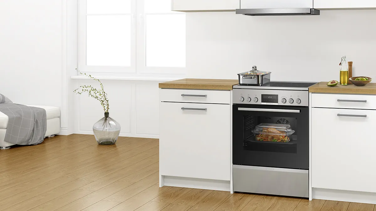 Electric freestanding cooker integrated into a white kitchen with wood flooring.