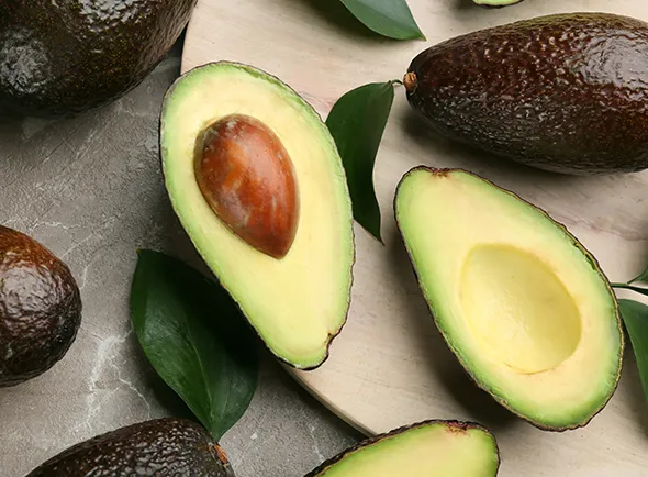 Ripe avocados, some halved to reveal their creamy green flesh and large pits.