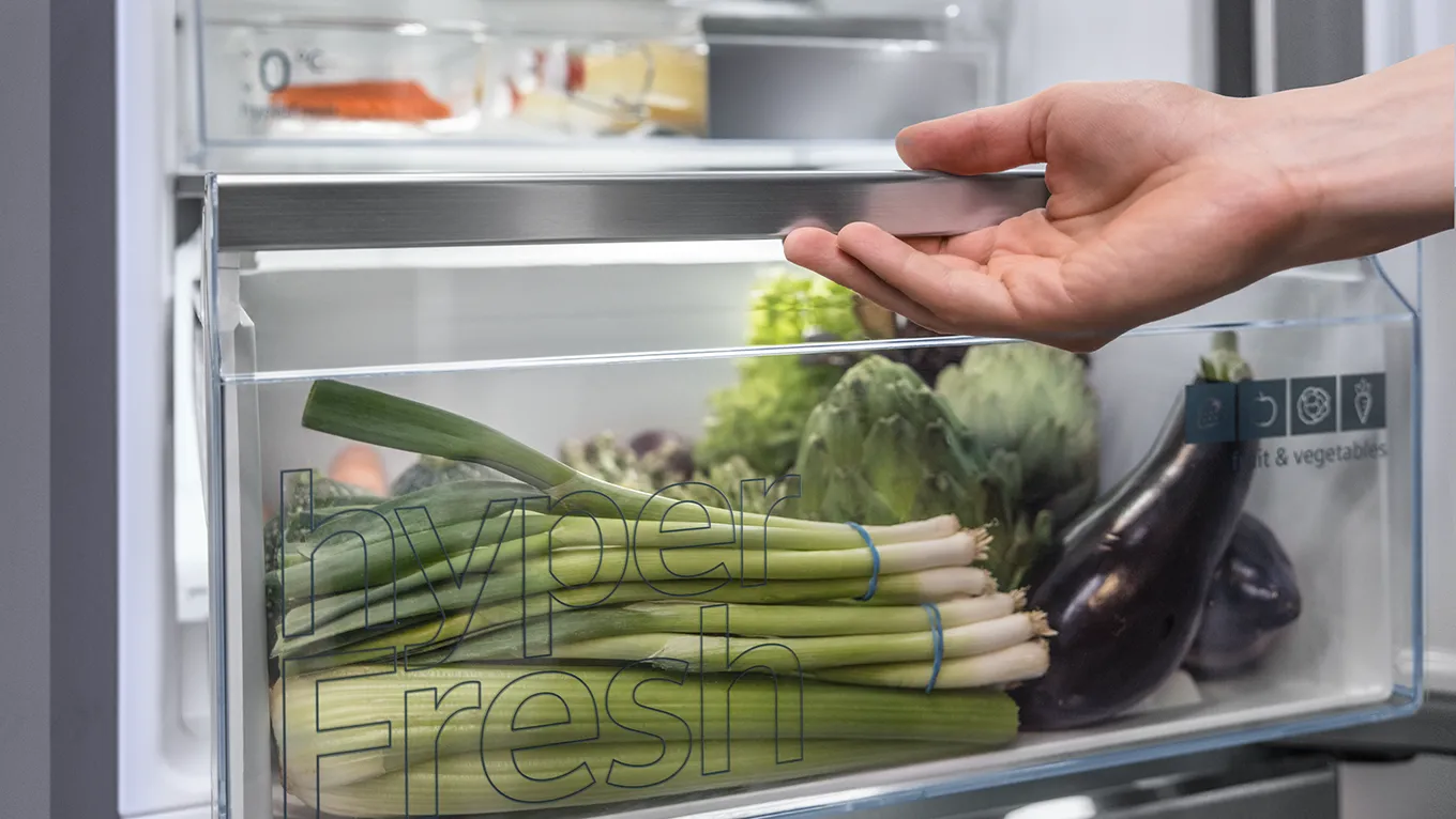 Gros plan sur une main ouvrant le tiroir hyperFresh rempli de légumes frais d'un réfrigérateur Siemens.